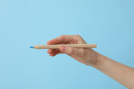 Female hand holding a pencil on a blue backgroundの写真素材
