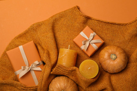 Candles, pumpkins and boxes on sweater on orange backgroundの写真素材