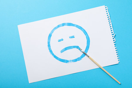 White paper with sad emoji and brush on blue background, top viewの写真素材