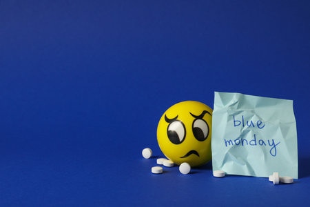 Note with text Blue Monday, pills and sad emoji on blue background, space for textの写真素材