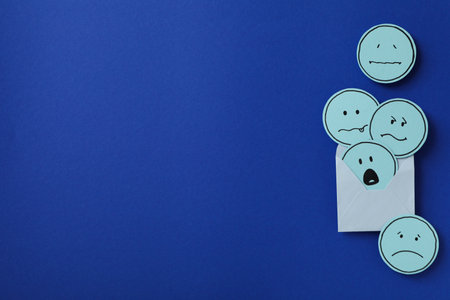 Envelope with sad emoji on blue background, space for textの写真素材