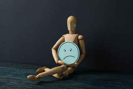 Wooden man with sad emoji in hands on dark blue backgroundの写真素材