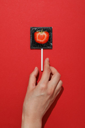 Black condom with strawberries on a red backgroundの写真素材