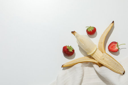 Condom on banana with strawberry on light background, place for textの写真素材
