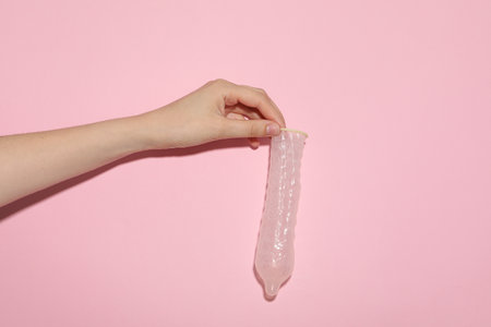 An unfolded condom in a hand on a pink backgroundの写真素材