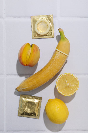 A condom on a banana with a peach and a lemon on a light backgroundの写真素材