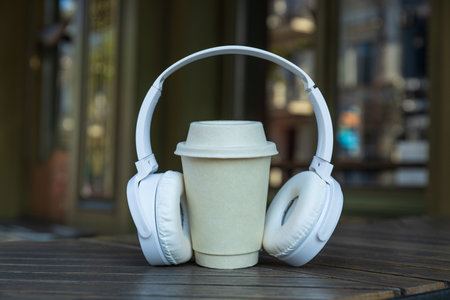 Paper cup and headphones on wooden table in coffee shop, close upの写真素材