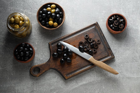 Olives in bowls and jar, kitchen board and knife on gray background, top viewの写真素材