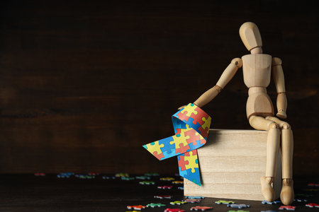 Ribbon with colorful puzzle pieces and wooden figure on dark background, place for text. world autism day conceptの写真素材
