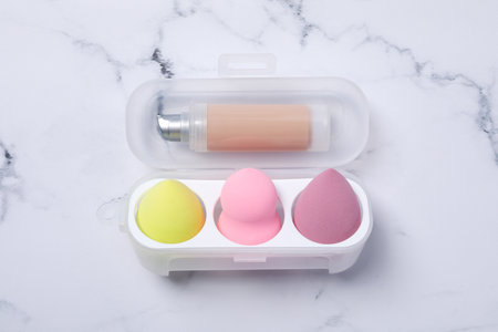 Cosmetic sponges in case and foundation on marble background, top viewの写真素材