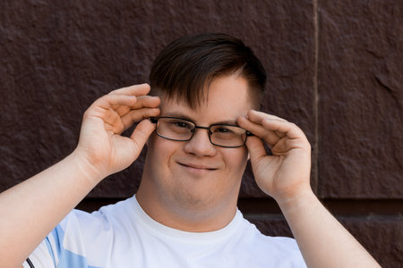Smiling young man with down syndrome in glasses posing against stone wall backgroundの写真素材