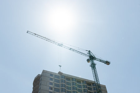 Tower cranes and unfinished buildings against a blue sky with white clouds.の写真素材