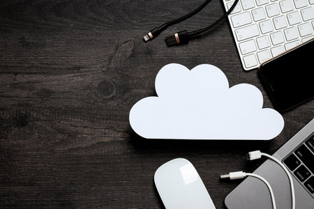 White, paper cloud with various gadgets on a black table background, place for textの写真素材