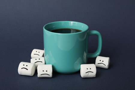 Cup and marshmallows with sad emoji on dark blue backgroundの写真素材