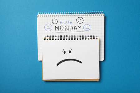 Notepads with text Blue Monday and sad emoji on blue background, top viewの写真素材