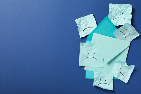 Envelopes and papers with sad emoji on blue background, space for textの写真素材
