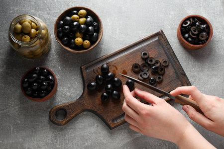 Jar and bowls with olives, kitchen board and female hands on gray background, top viewの写真素材
