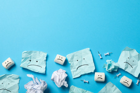 Papers and marshmallows with sad emoji on blue background, space for textの写真素材