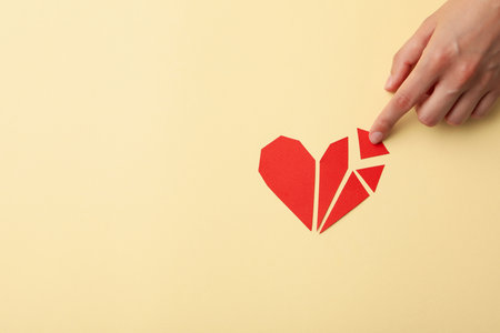 Red heart made of paper particles with a hand on a light background. Blood donation, place for text