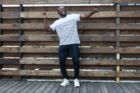 A stylish, young African-American man poses for the camera against the background of a wooden fenceの写真素材