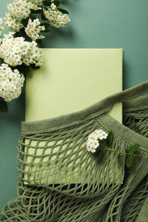 Book in string bag and flowers on green background, top viewの写真素材