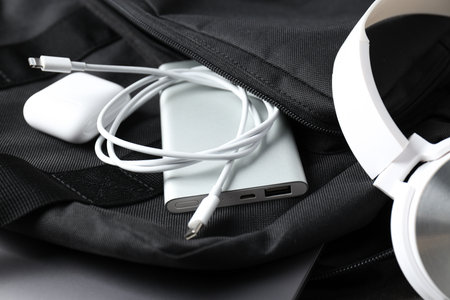 Powerbank and wireless headphones in backpack pocket on white background, close up