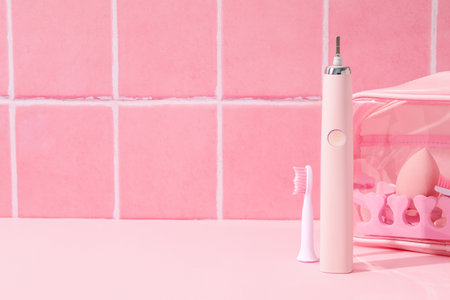 Electric toothbrush and cosmetic bag on pink background, space for textの写真素材
