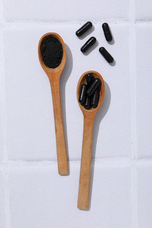 Activated charcoal tablets with wooden spoons on a light backgroundの写真素材