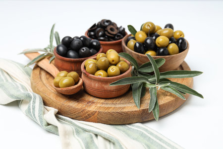 Olives in bowls and spoon on wooden stand on white background, close upの写真素材