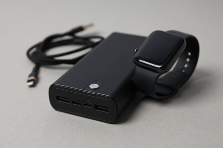 Powerbank, cord and smart clock on gray background, close up
