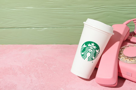 Ukraine, Kyiv, 08/24/2023: Starbucks coffee cup with logo, with phone.のeditorial素材