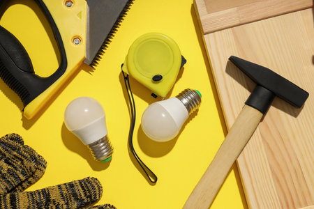 Construction tools and light bulbs on yellow background, top view