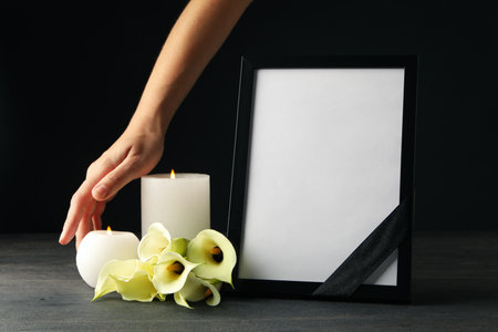 Photo frame with black ribbon, candles, flowers and female hand on black backgroundの写真素材