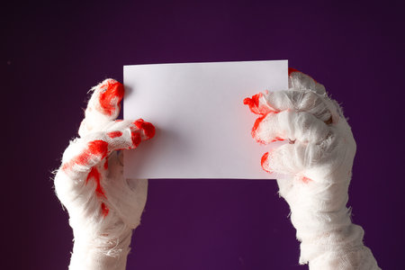 Hands wrapped in a bandage hold a blank piece of paperの写真素材