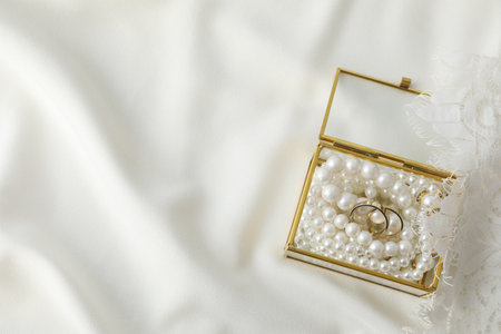 Golden wedding rings in jewelry box with pearls on white background, space for text