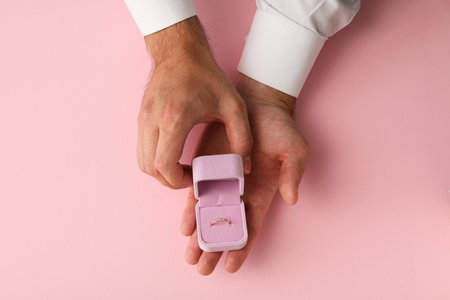 Golden wedding ring in case in male hands on pink background, top view