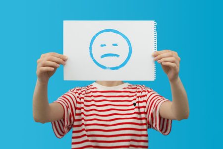 Woman with album sheet with sad emoji on blue backgroundの写真素材