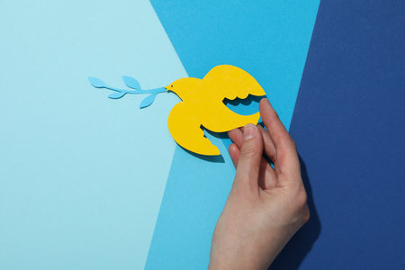 Decorative paper bird in hand on blue background, top viewの写真素材