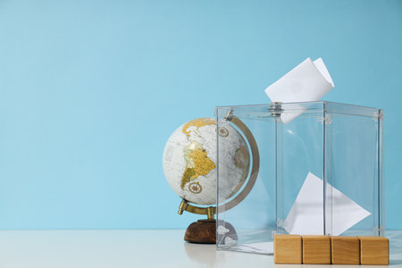 Voting box with papers, wooden cubes and globe on blue background, space for textの写真素材
