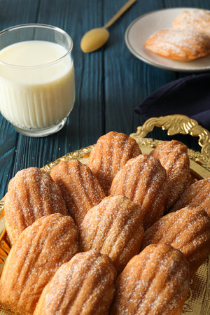 Madeleine cakes and glass of milk on blue wooden background, close up