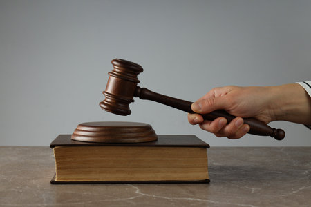 Book and judge's gavel in hand on gray backgroundの写真素材