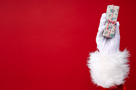 Gift box in Santa's hand on red background, space for textの写真素材