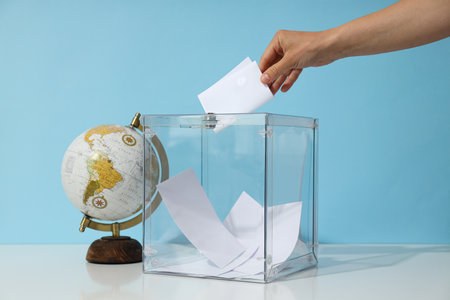 Voting box with papers, hand and globe on blue backgroundの写真素材