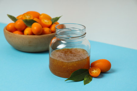 Kumquat in bowl and jar of jam on blue table on white backgroundの写真素材