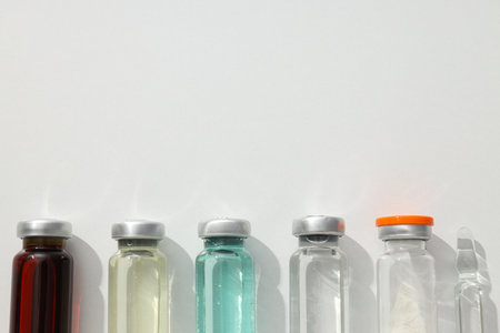 Glass medical bottles and ampoule with vaccine on white background, space for text