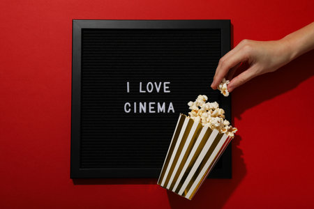 Letter board with text, popcorn in paper cup and hand on red background, top viewの写真素材