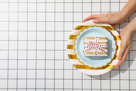 Plates and gift box in hands on light background, space for textの写真素材