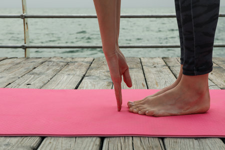 Female hands and feet on pink yoga mat on wooden floor outdoors, close upの写真素材