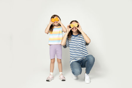 Mother and daughter are joking with oranges instead of eyes, on a gray background.の写真素材