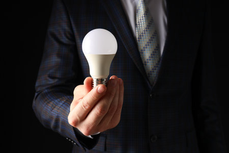 A businessman's hand holds a light bulb on a black backgroundの写真素材